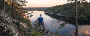 Mies katsoo korkealta avautuvaa järvimaisemaa, vastarannalla metsäinen kallio.